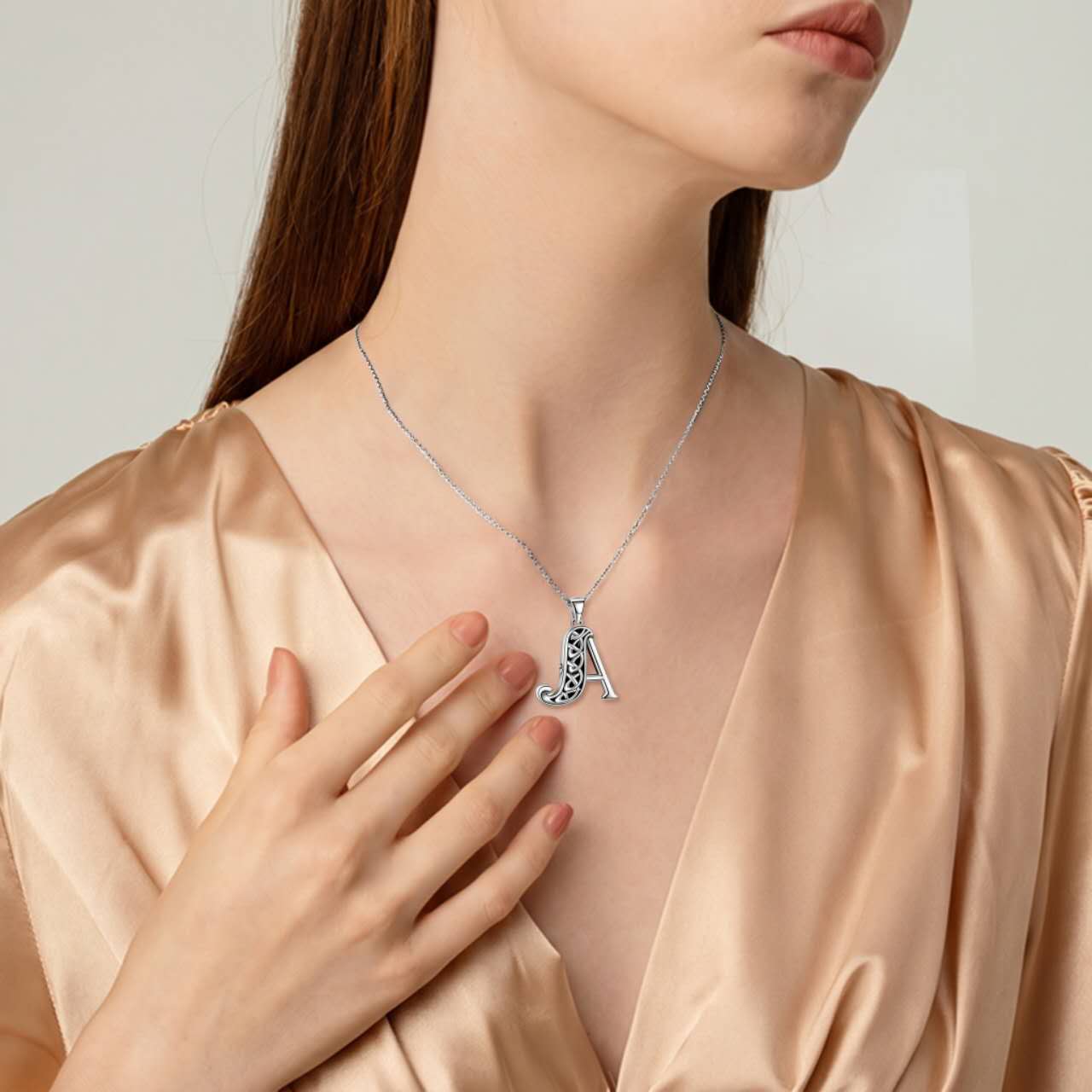 Woman wearing a necklace with the letter A cremation pendant on a plain background