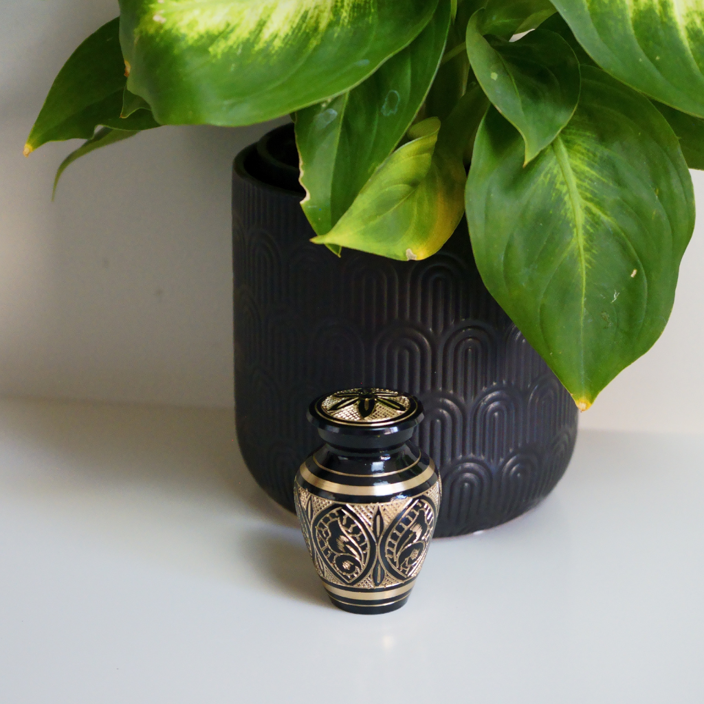 Brass keepsake urn with intricate butterfly details in natural setting