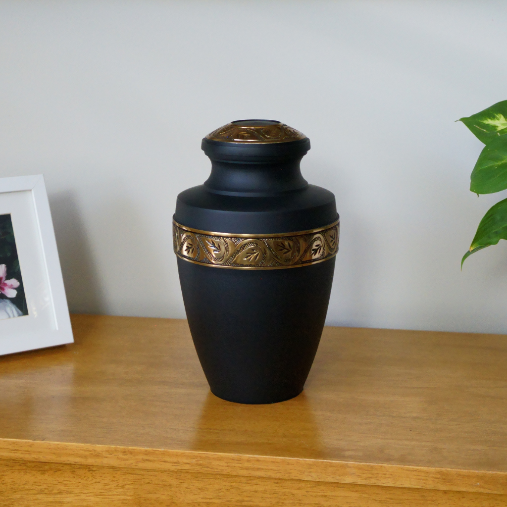 Matte black urn with gold stripe and leaf details in natural setting
