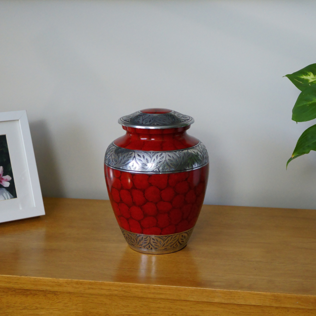 Red urn with soft scale details and silver leafy accents in natural setting