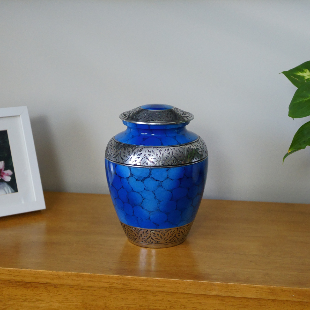 Blue urn with soft scale details and silver leafy accents in natural setting