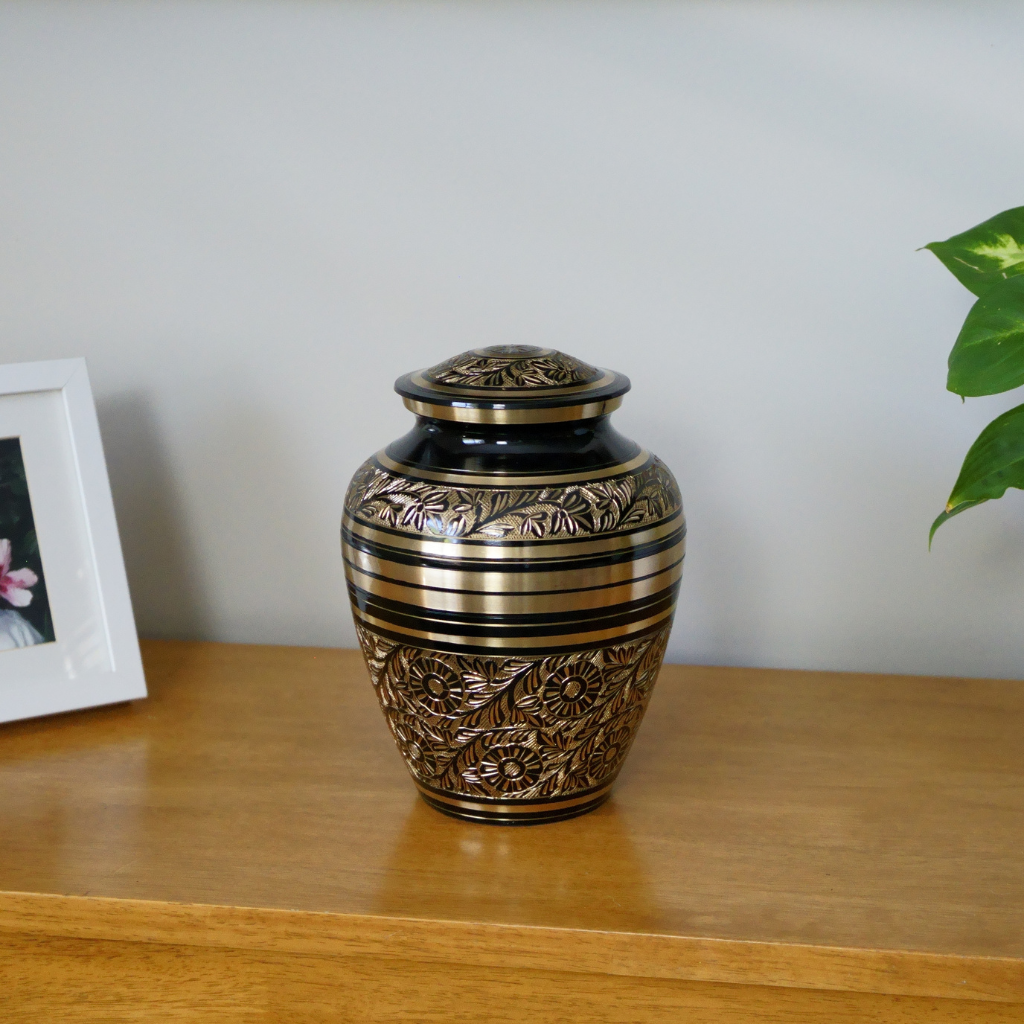 Black and gold brass urn with floral and nature patterns in natural setting