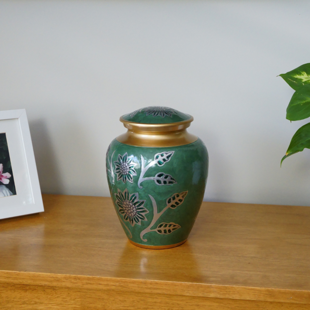 Green and gold urn with silver detailed floral patterns in natural setting