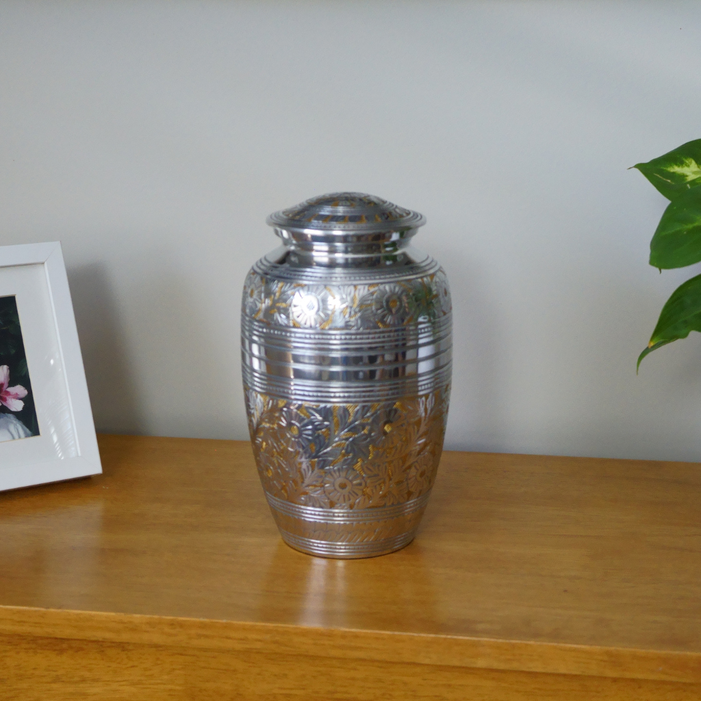 Silver and gold brass urn with intricate flower details in natural setting