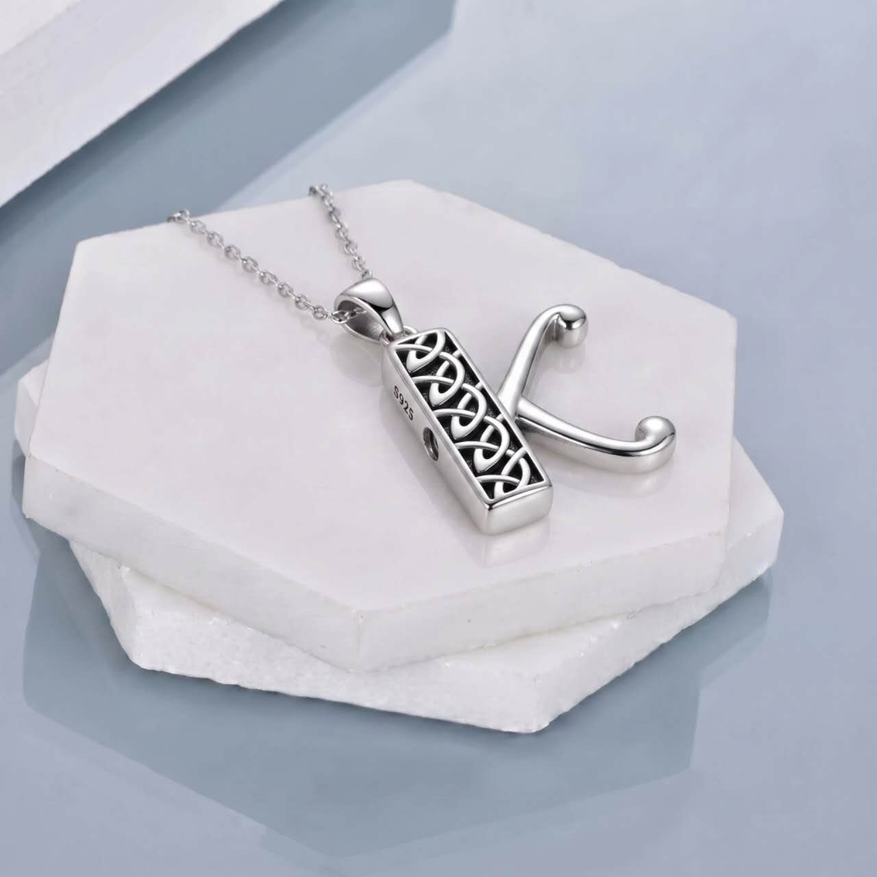 A silver cremation pendant necklace displayed on a white hexagonal stone stand.