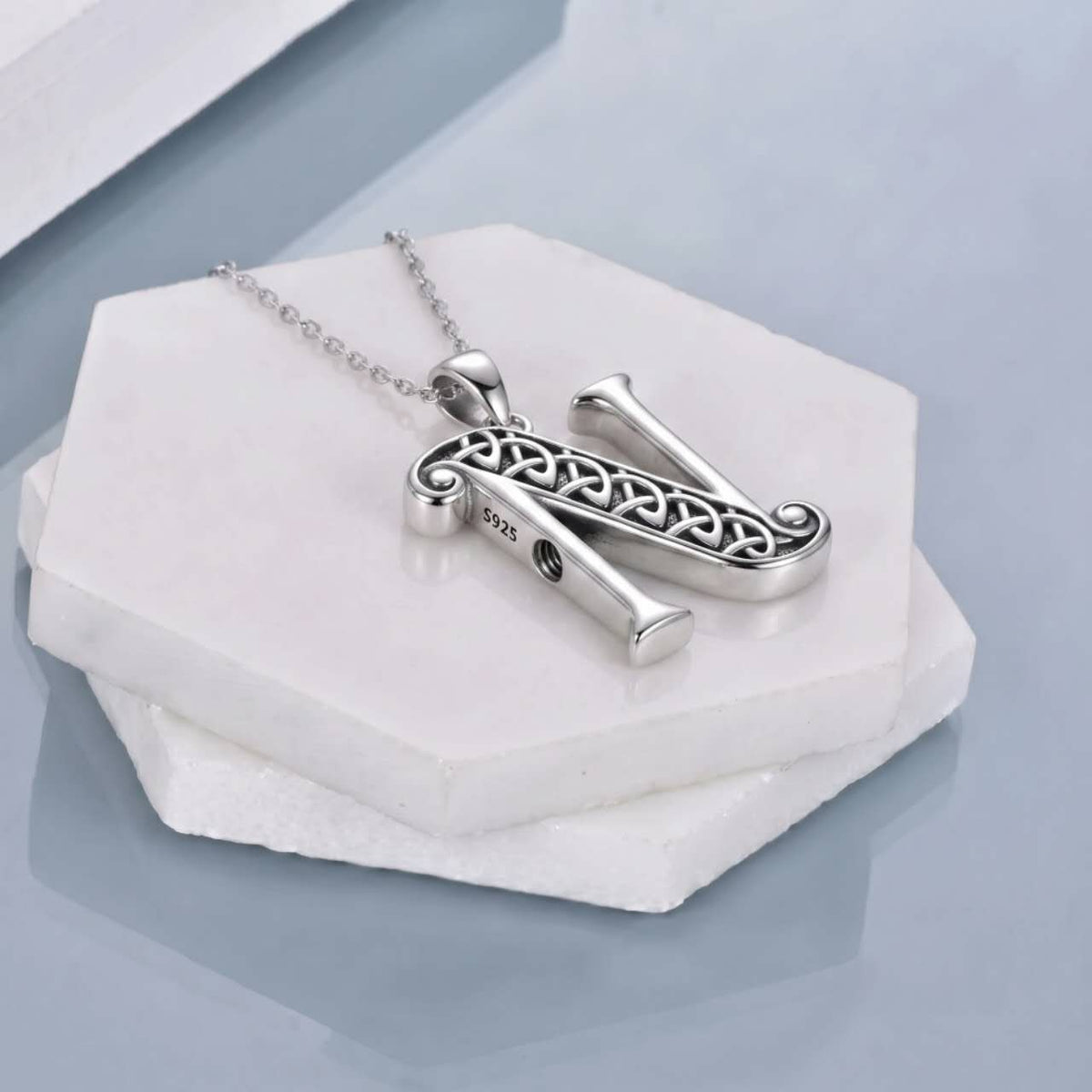 A silver-toned necklace with the letter N, featuring an intricate Celtic knot pattern on a white hexagonal stone block.
