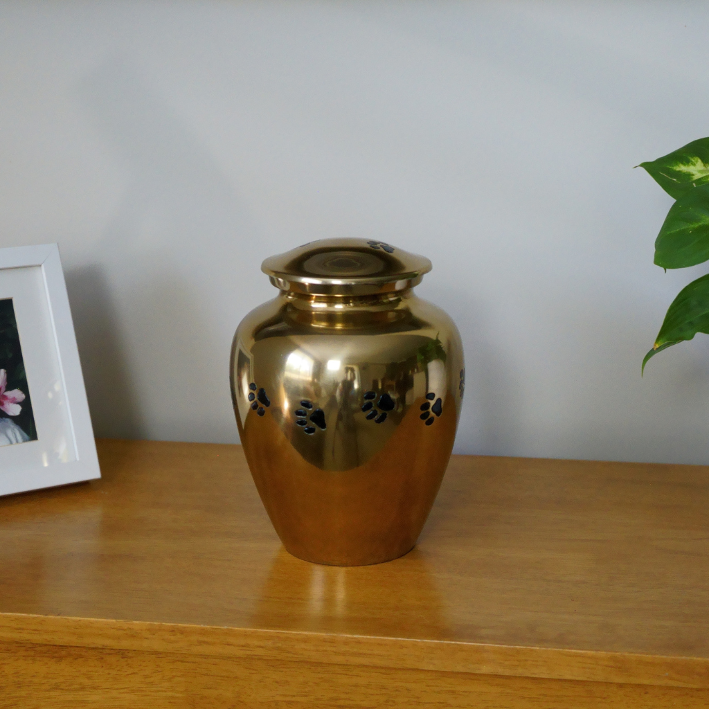 Gold urn with black etched pawprints in natural setting