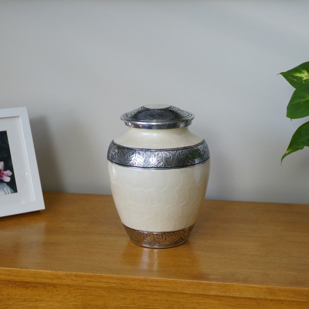 White soft scale urn with silver leaf details in natural setting