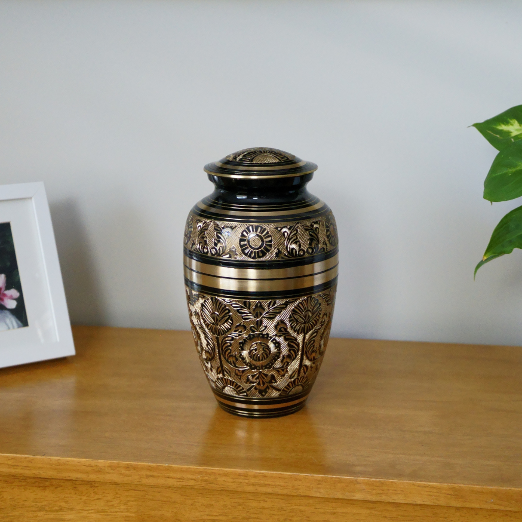 Black and gold brass urn with flower and nature details in natural setting