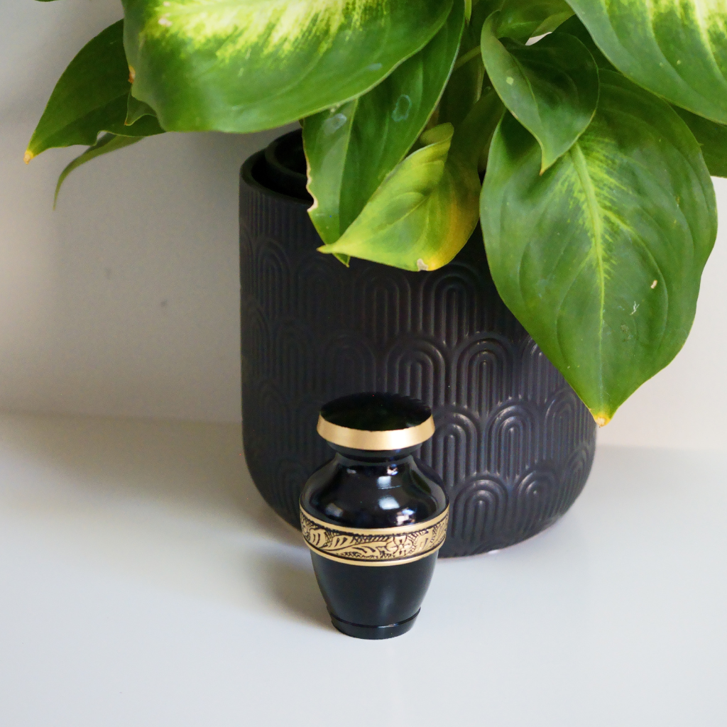 Black keepsake urn with gold leaf and flower detailing in natural setting