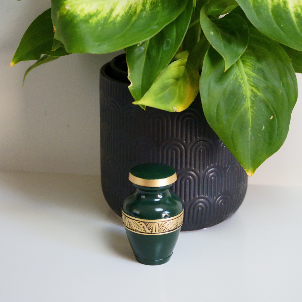 Green keepsake urn with gold leaf details in natural setting