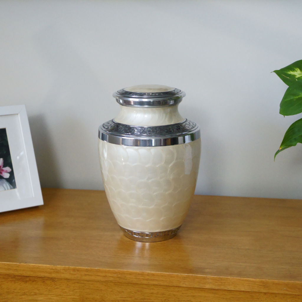 White soft scale urn with silver leaf details in natural setting