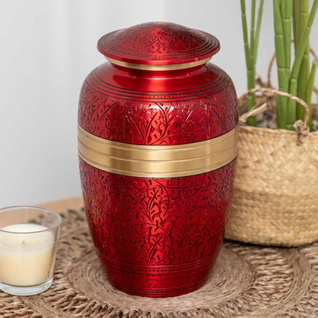 Red aluminium urn with intricate engravings and a gold detail in natural setting