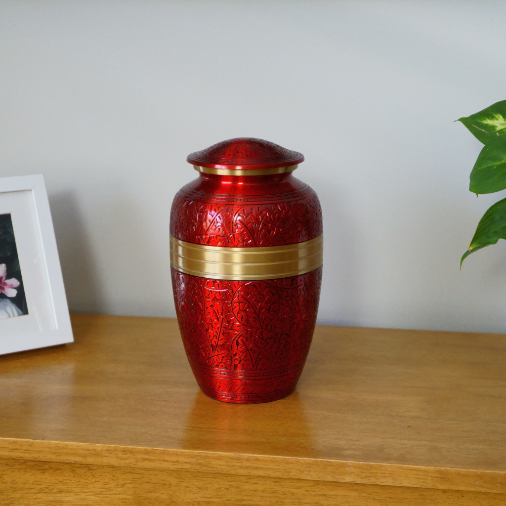 Red aluminium urn with intricate engravings and a gold detail in natural setting