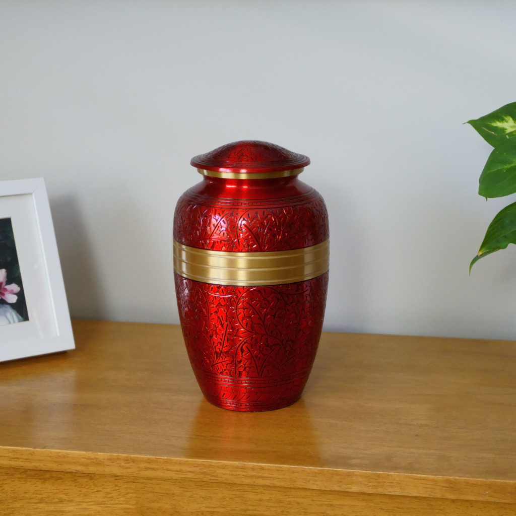 Red brass urn with intricate engravings and a gold detail in natural setting