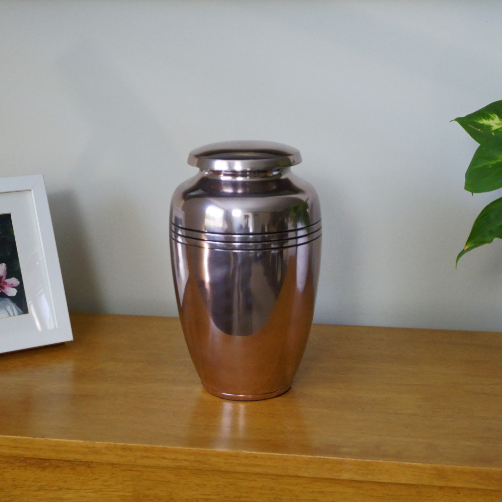 Slightly pink metallic urn with 3 black line details in natural setting