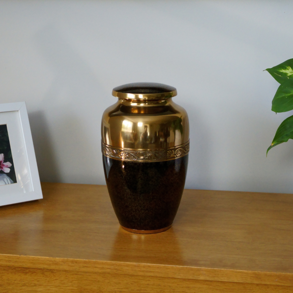 Brass urn with black speckled details on the bottom half in natural setting