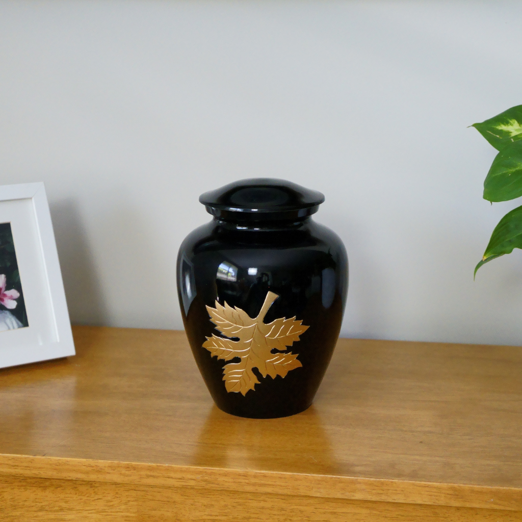 Black urn with gold autumn leaf etched in natural setting